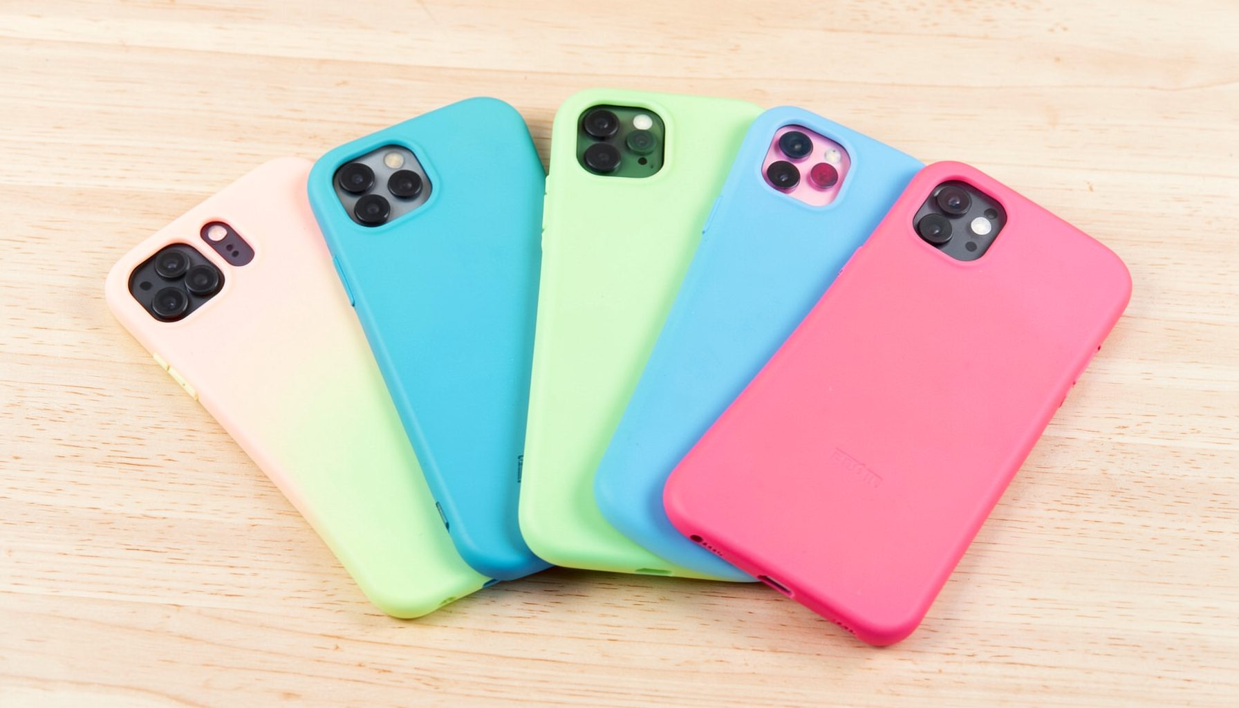 Several colorful phone cases arranged in a fan pattern on a light wood table, bright and playful product-display style.