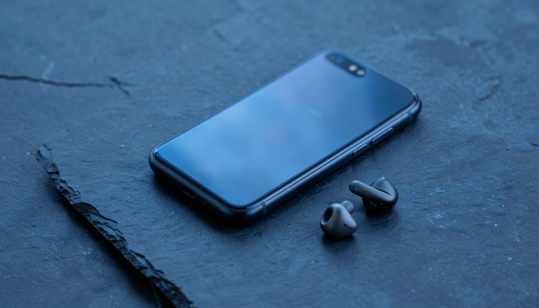 A sleek modern smartphone and wireless earbuds resting on a dark slate surface, with soft blue and charcoal tones.